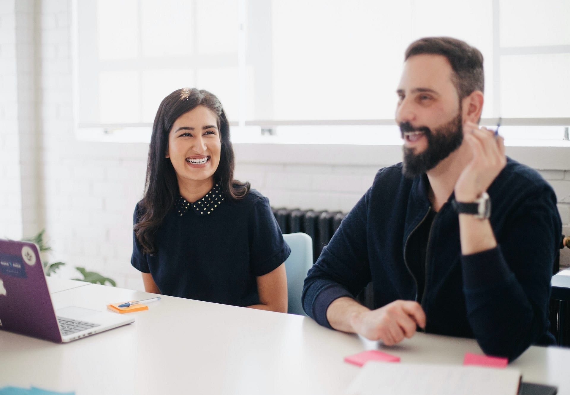 Two colleagues smiling in a meeting, a laptop and notes on the table